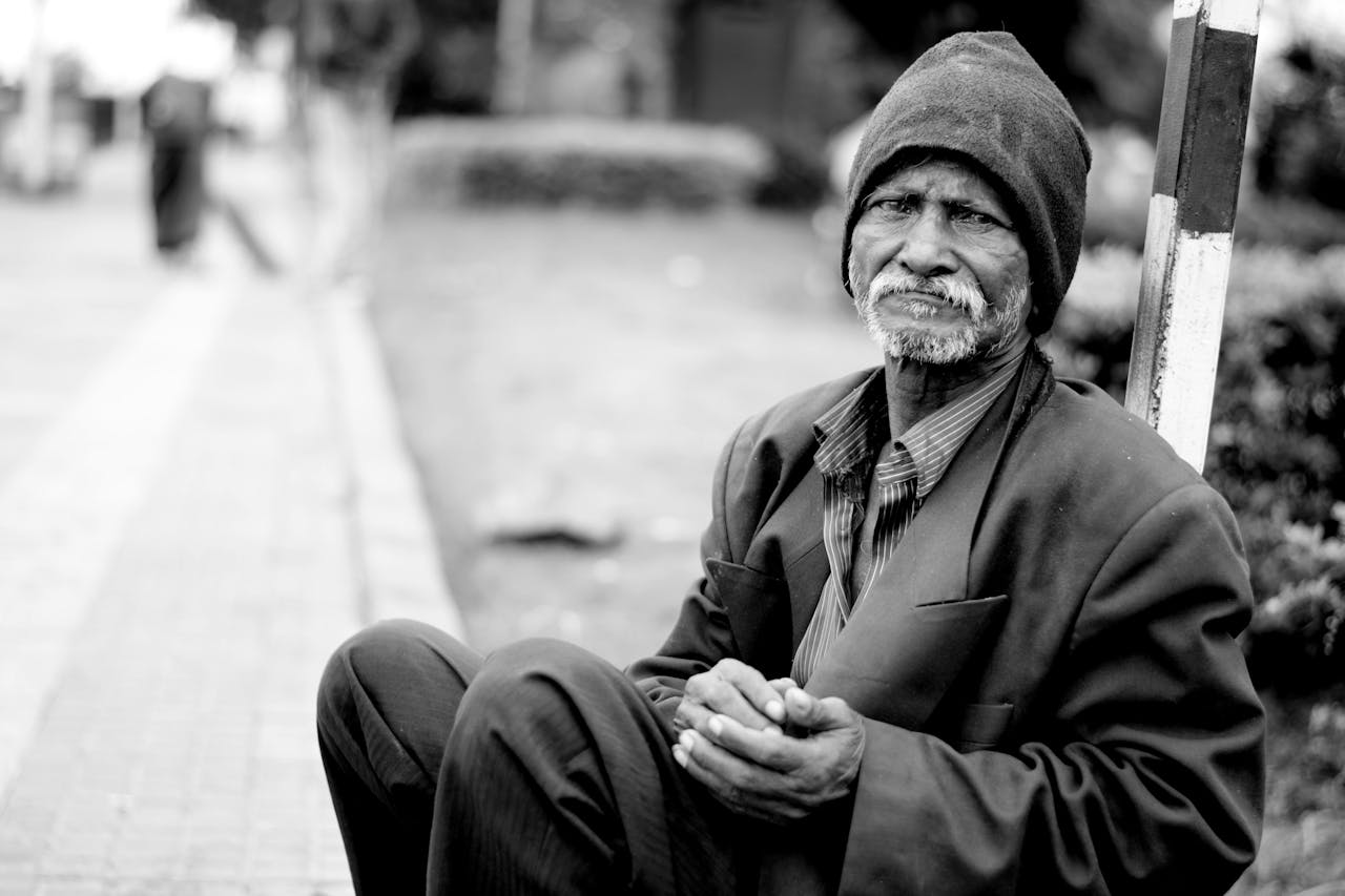 services-01 A black and white portrait of an elderly man sitting on the streets, expressing hardship and resilience.